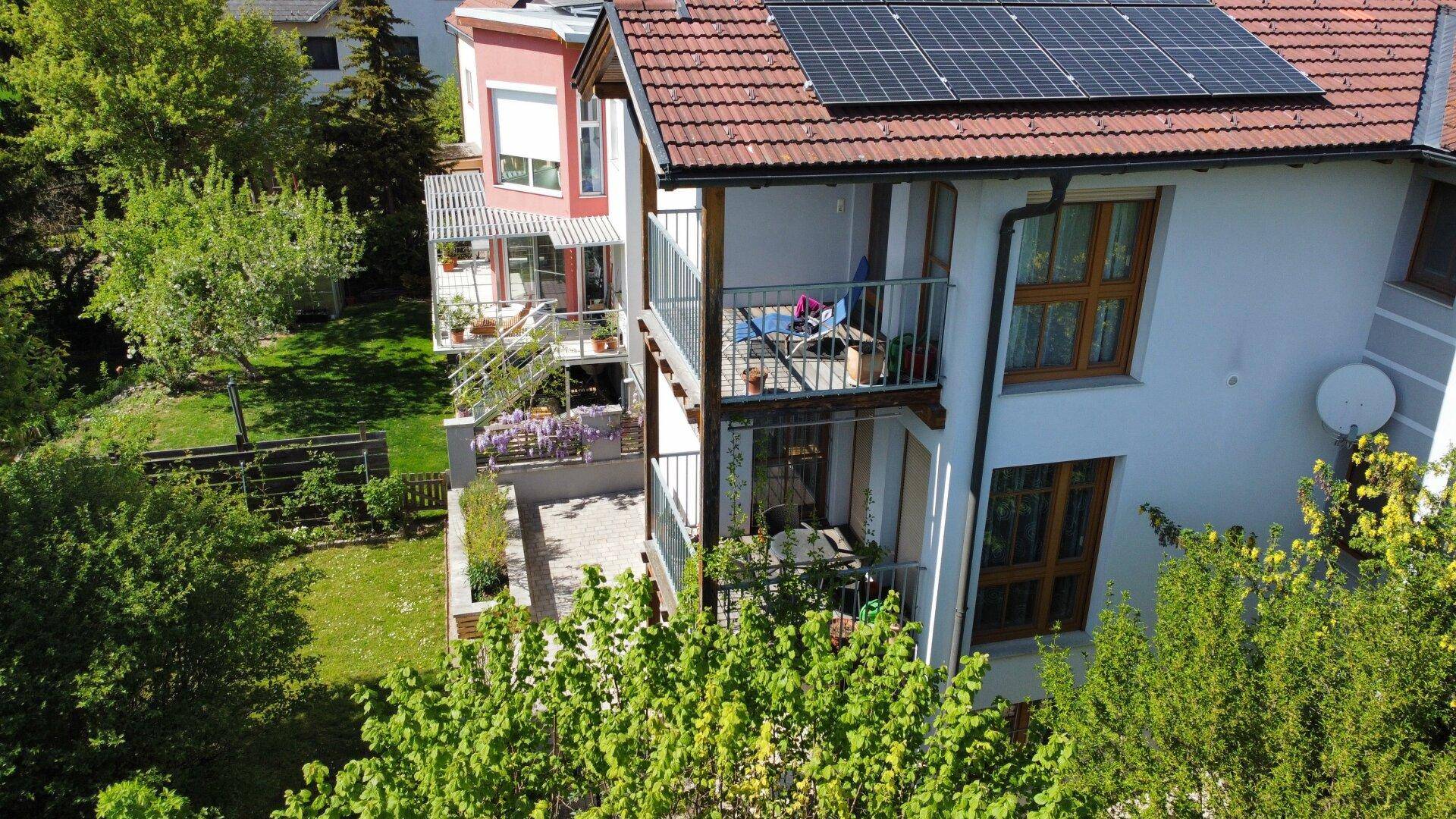 Fassade des Hauses mit zwei Balkonen, einer Terrasse und Photovoltaikmodulen auf dem Dach.
