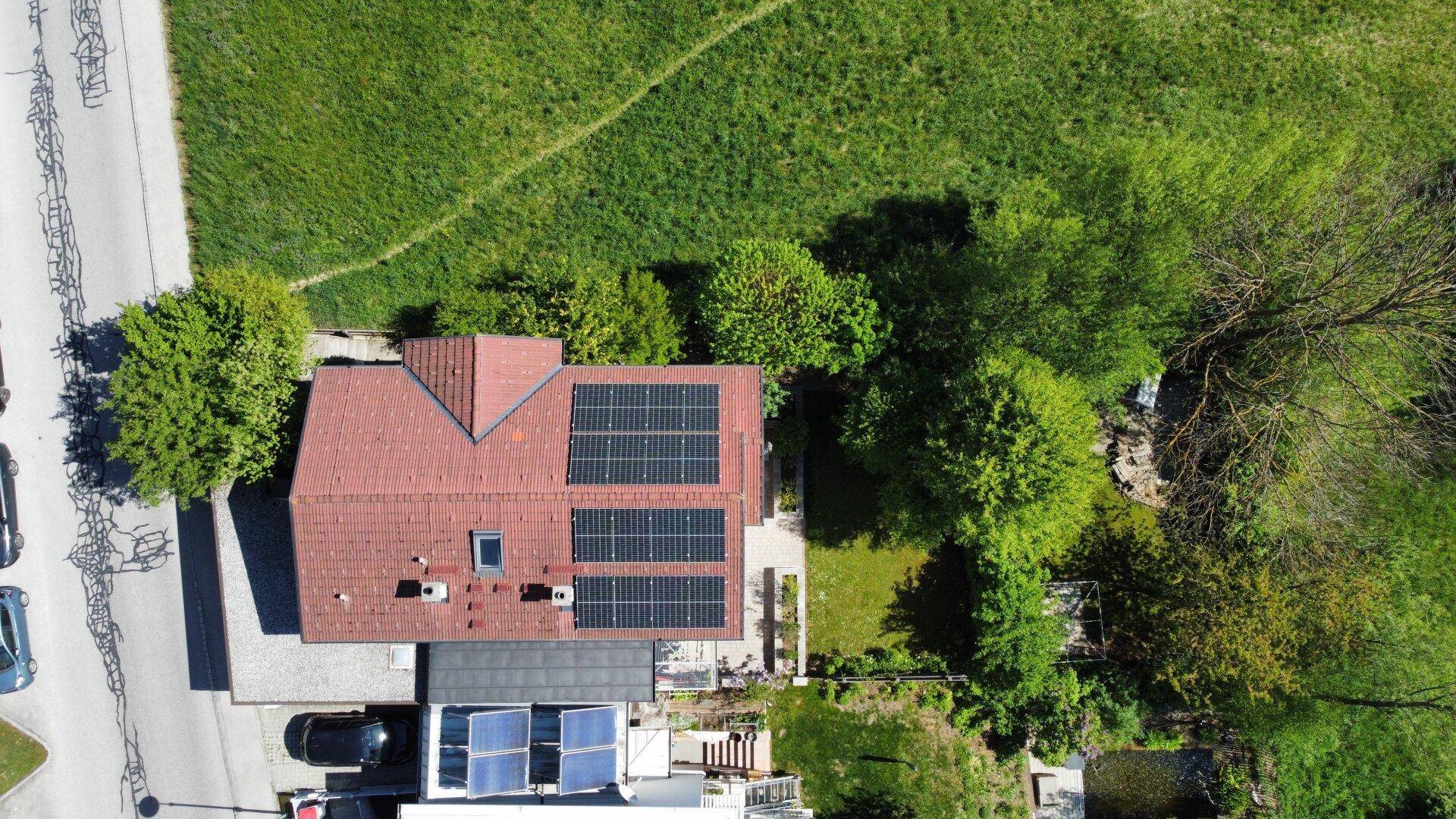 Senkrechte Luftaufnahme des Hauses mit Photovoltaikanlage, Garten und angrenzender Grünfläche.