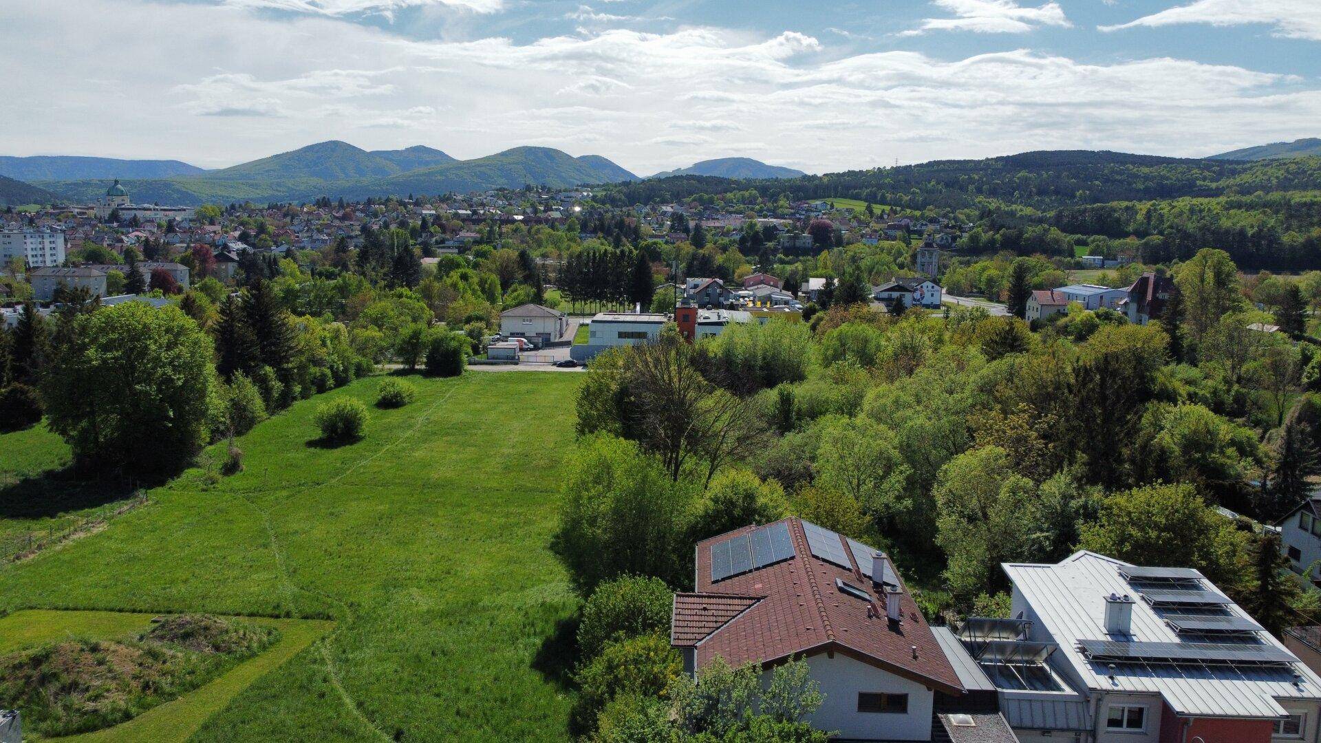 Weitläufige Luftaufnahme der Immobilie mit Photovoltaikanlage, umgeben von Stadt und grüner Hügellandschaft.
