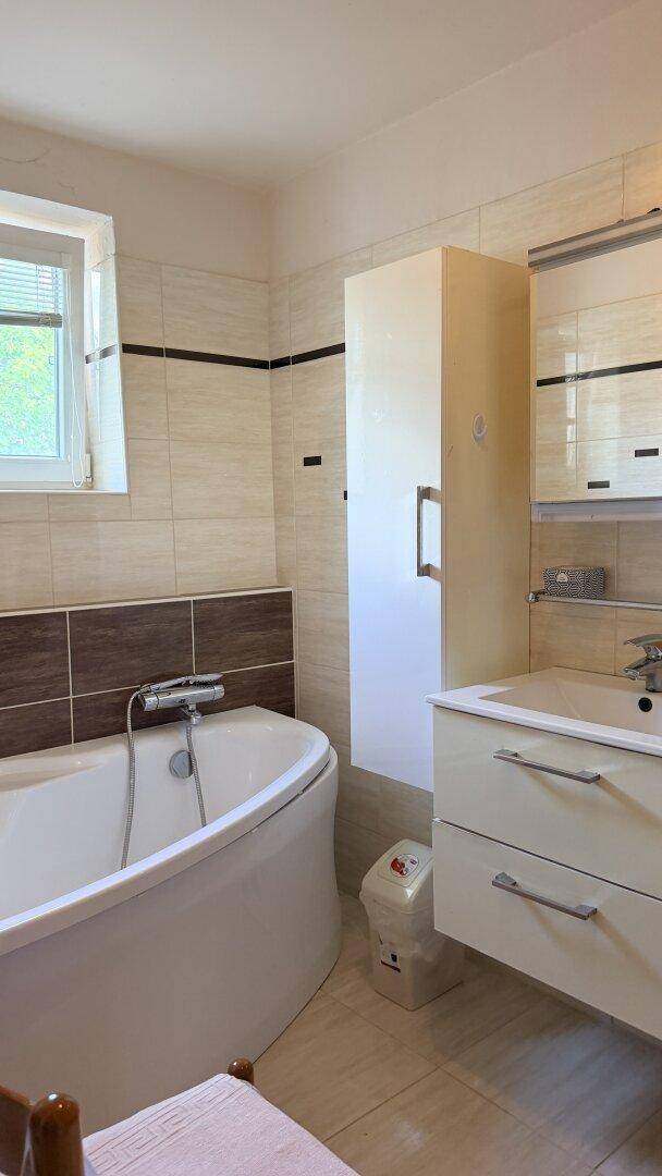Badezimmer mit Badewanne, Waschtisch und Fliesen in hellen und dunklen Brauntönen.