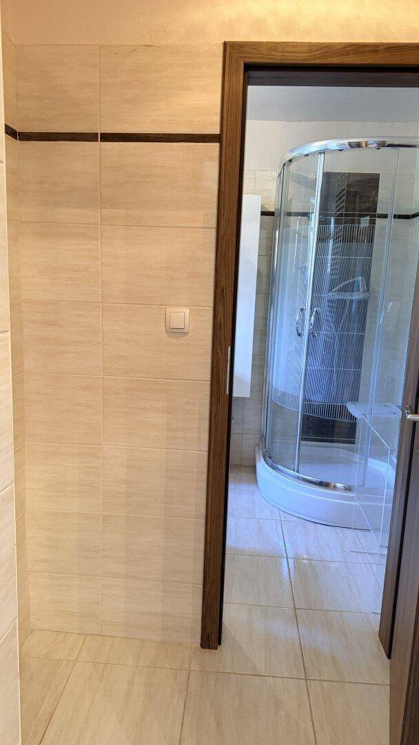Badezimmer mit Duschkabine und hellen Fliesen an Wänden und Boden.