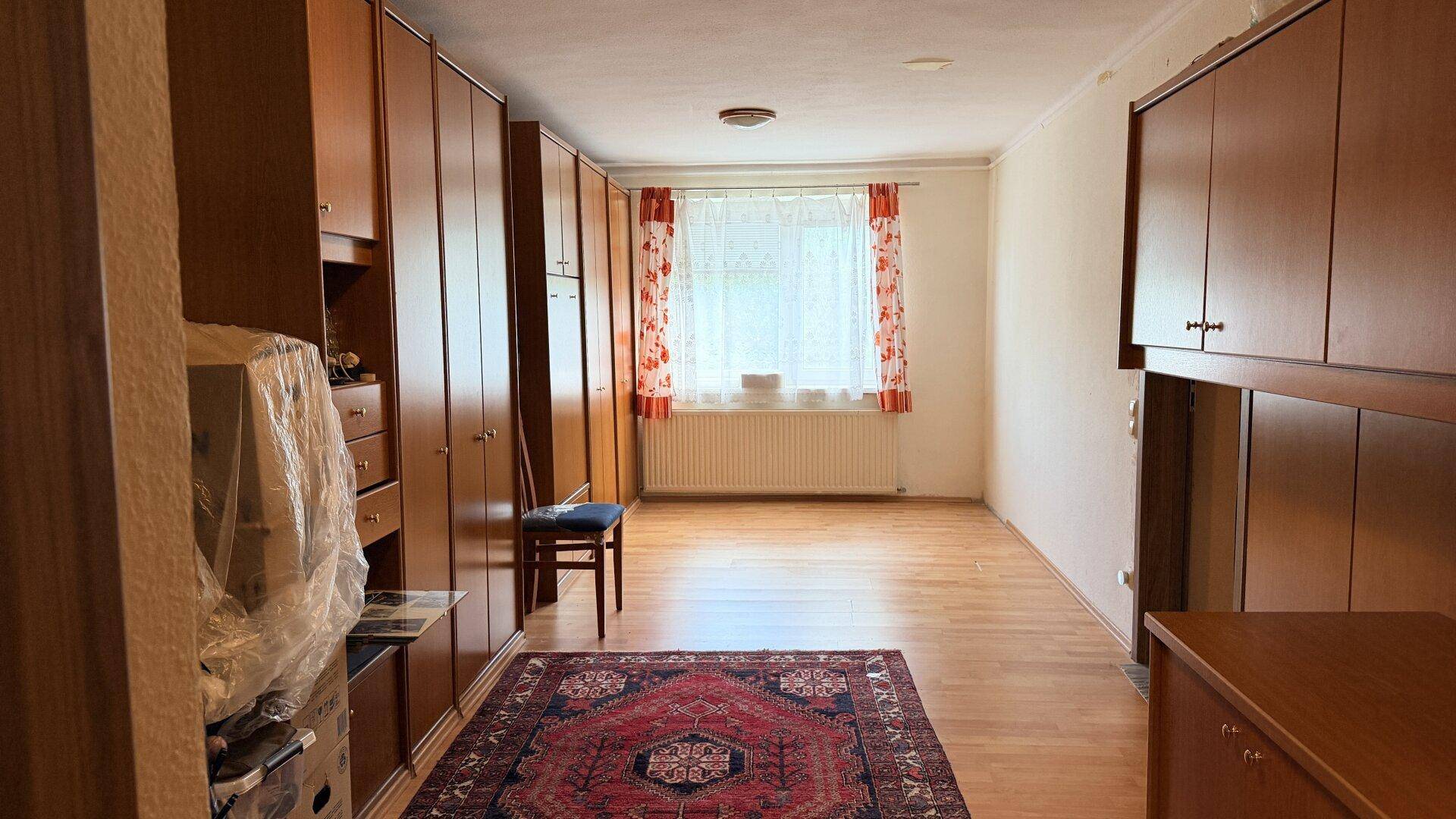 Geräumiges Zimmer mit Einbauschränken, Holzboden und Fenster mit Vorhängen.