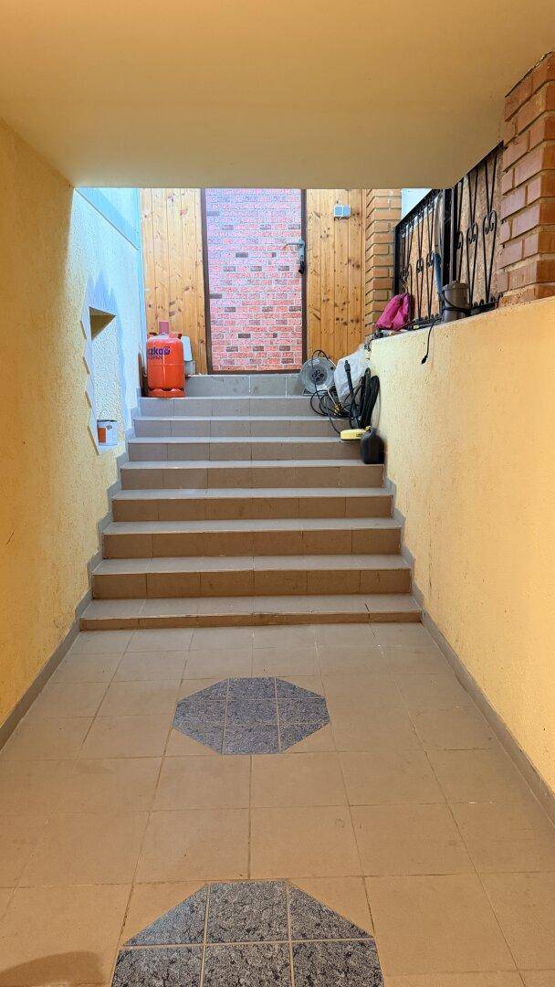 Eingangsbereich mit gefliestem Boden und Treppe, die zu einer Holztür führt.