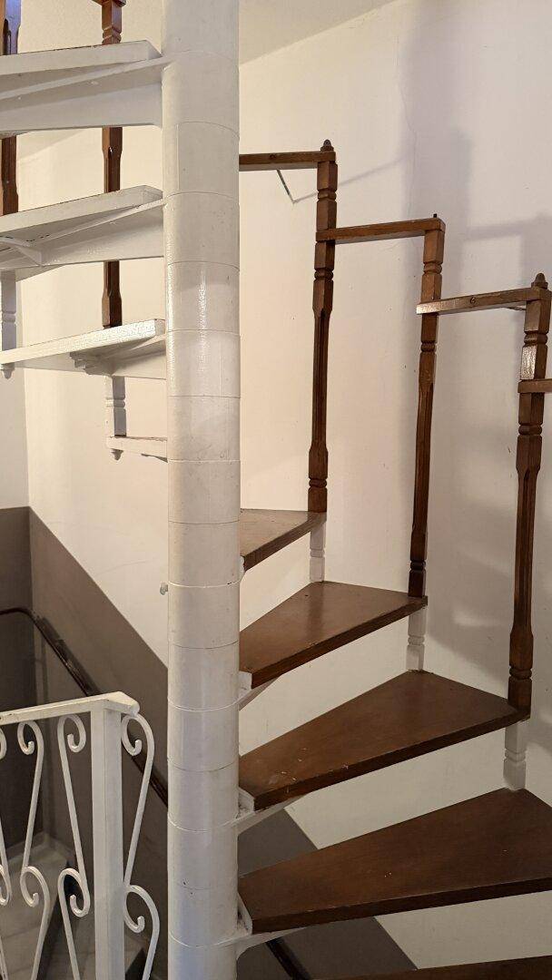 Wendeltreppe mit Holzstufen und weißem Metallgeländer in einem Innenraum.