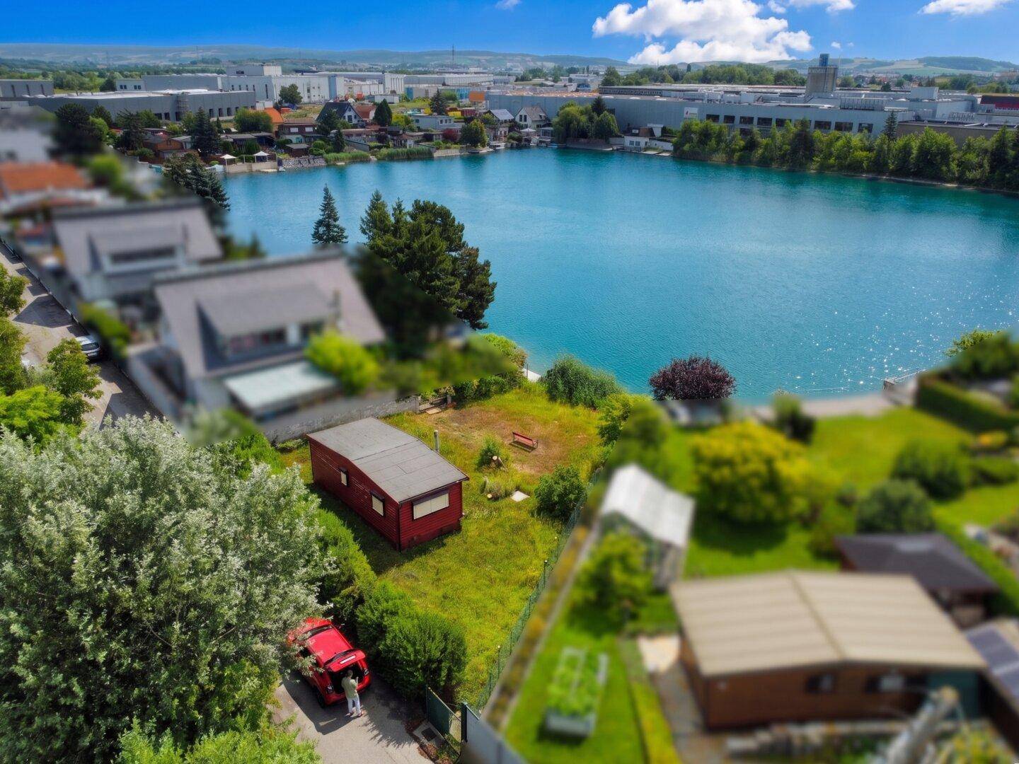 Weitläufige Luftaufnahme eines Grundstücks am See mit angrenzenden Gebäuden und viel Grün.