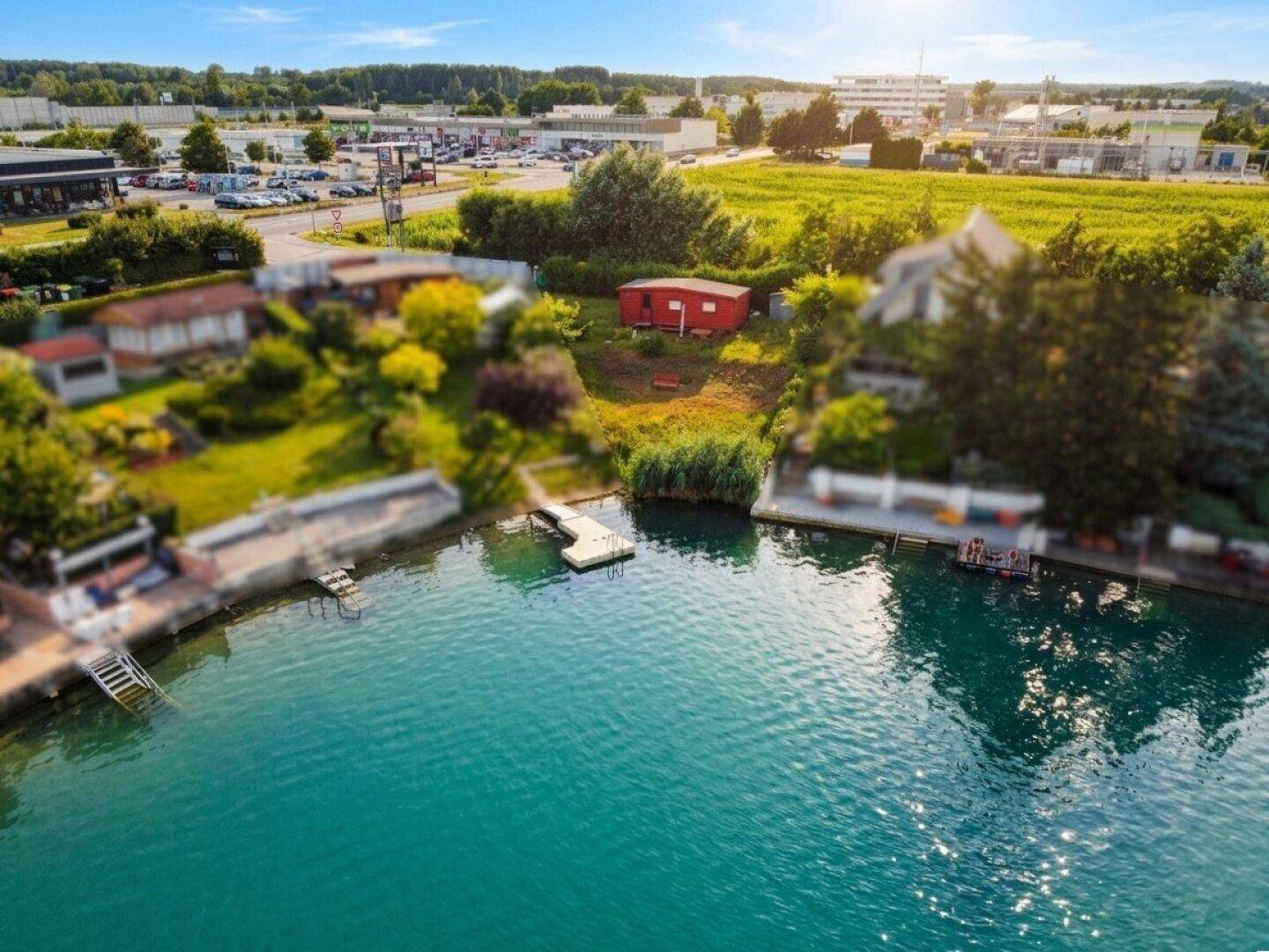 Panoramablick aus der Luft auf ein Seegrundstück mit rotem Haus, Steg und weiteren Anwesen.