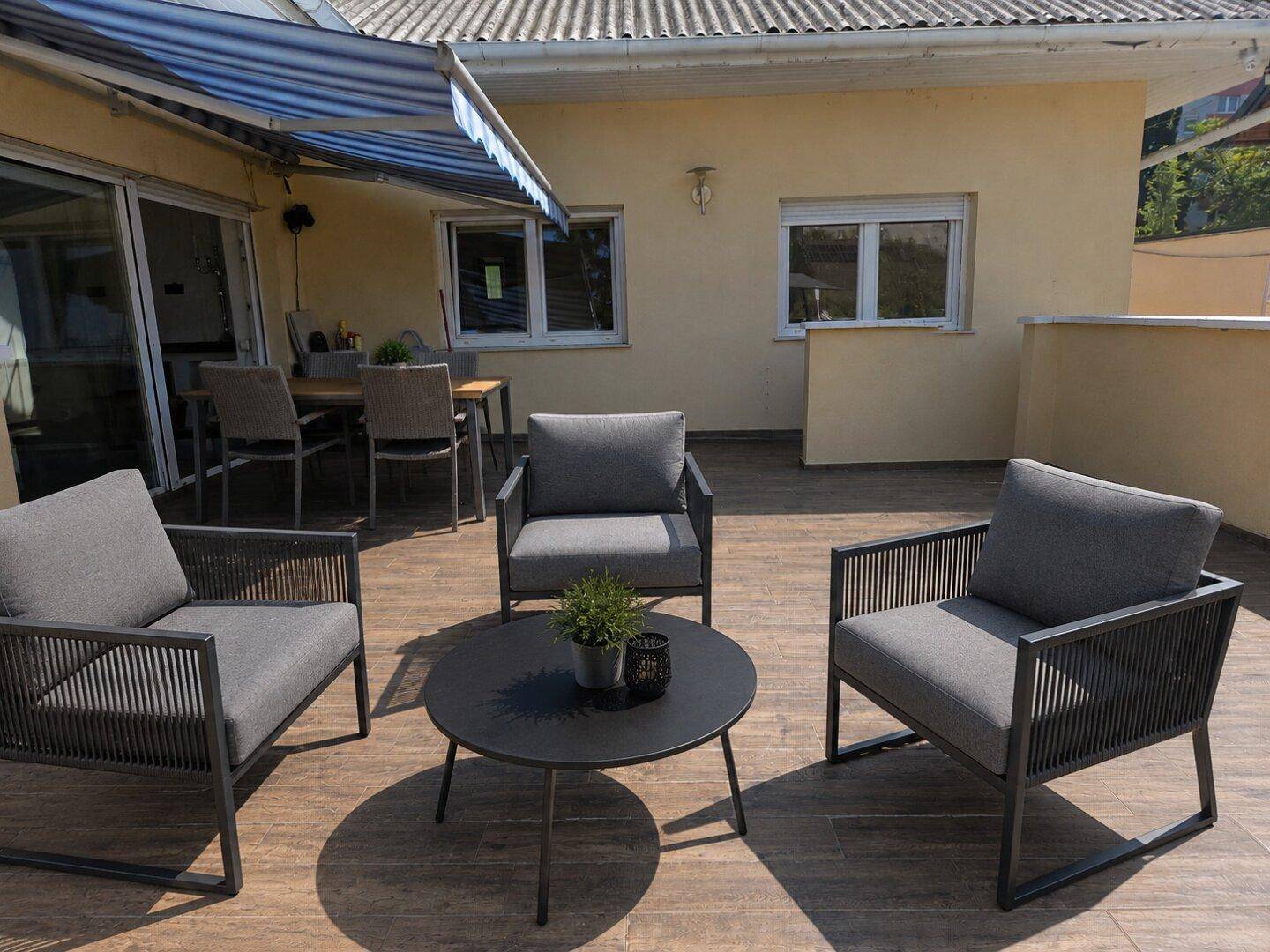 Geräumige Terrasse mit modernen Outdoor-Sesseln, Couchtisch und Markise für Schatten.