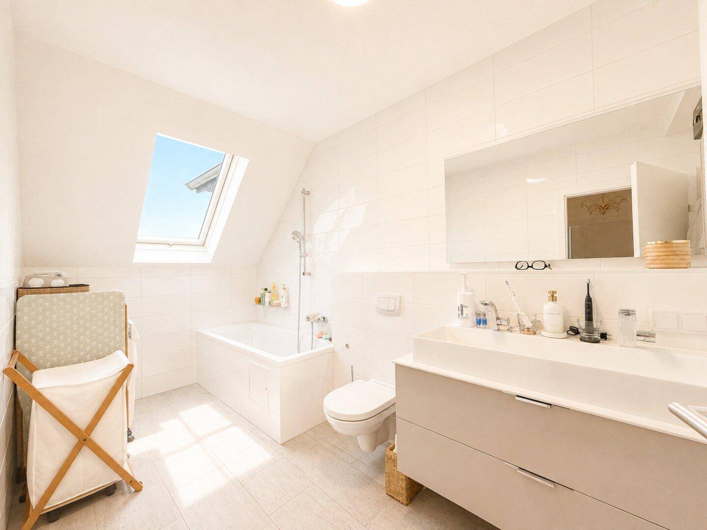 Modernes Badezimmer mit Badewanne, großem Waschtisch und Dachfenster für viel Licht.