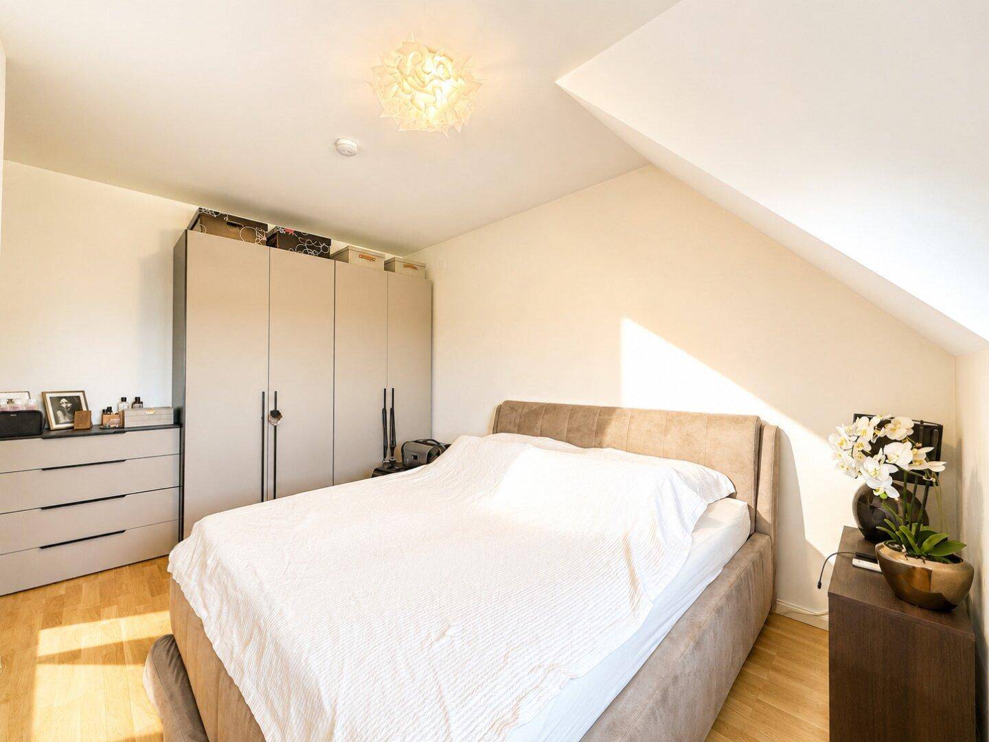 Helles Schlafzimmer mit großem Bett, Einbauschränken und schrägen Wänden unter dem Dach.
