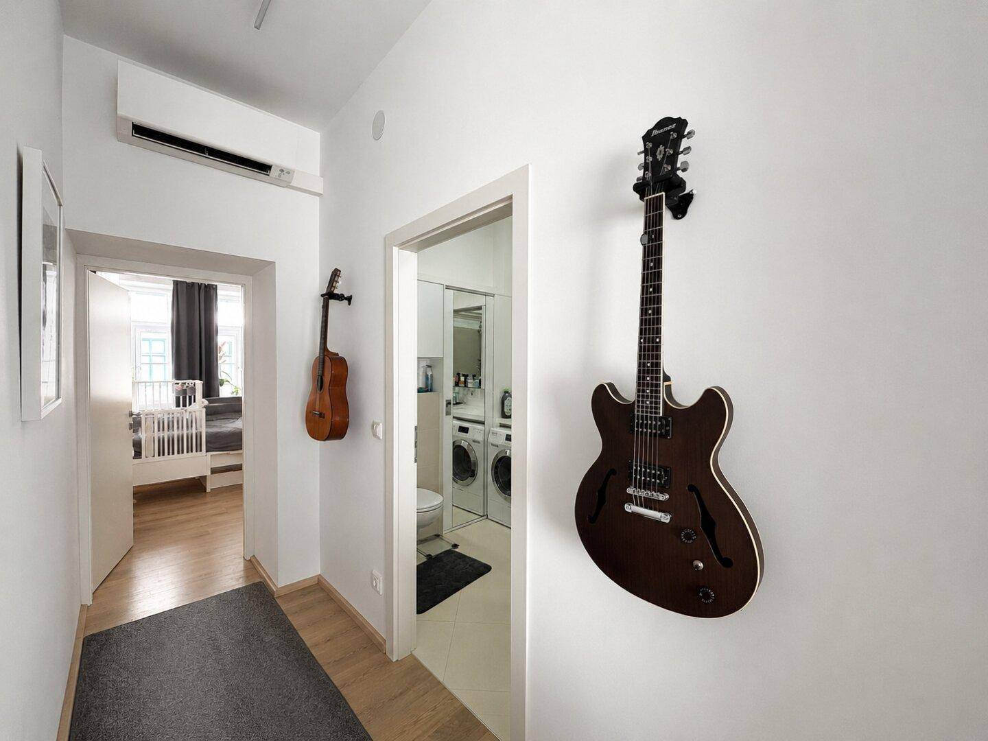 Heller Flur mit Gitarren an der Wand und Zugang zu Schlafzimmer und Waschküche.