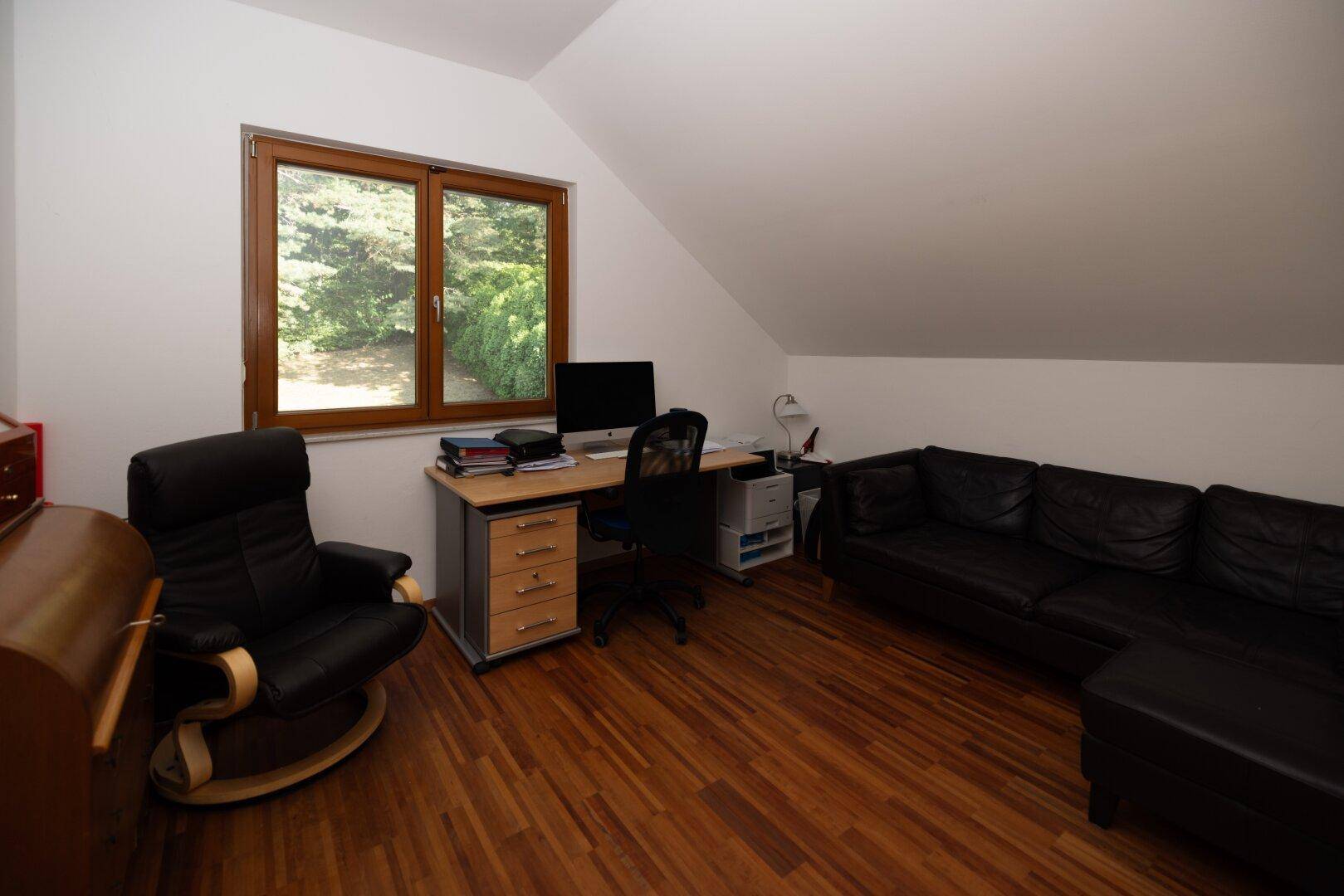 Helles Arbeitszimmer mit Holzfußboden, Schreibtisch und bequemer Sitzgelegenheit.