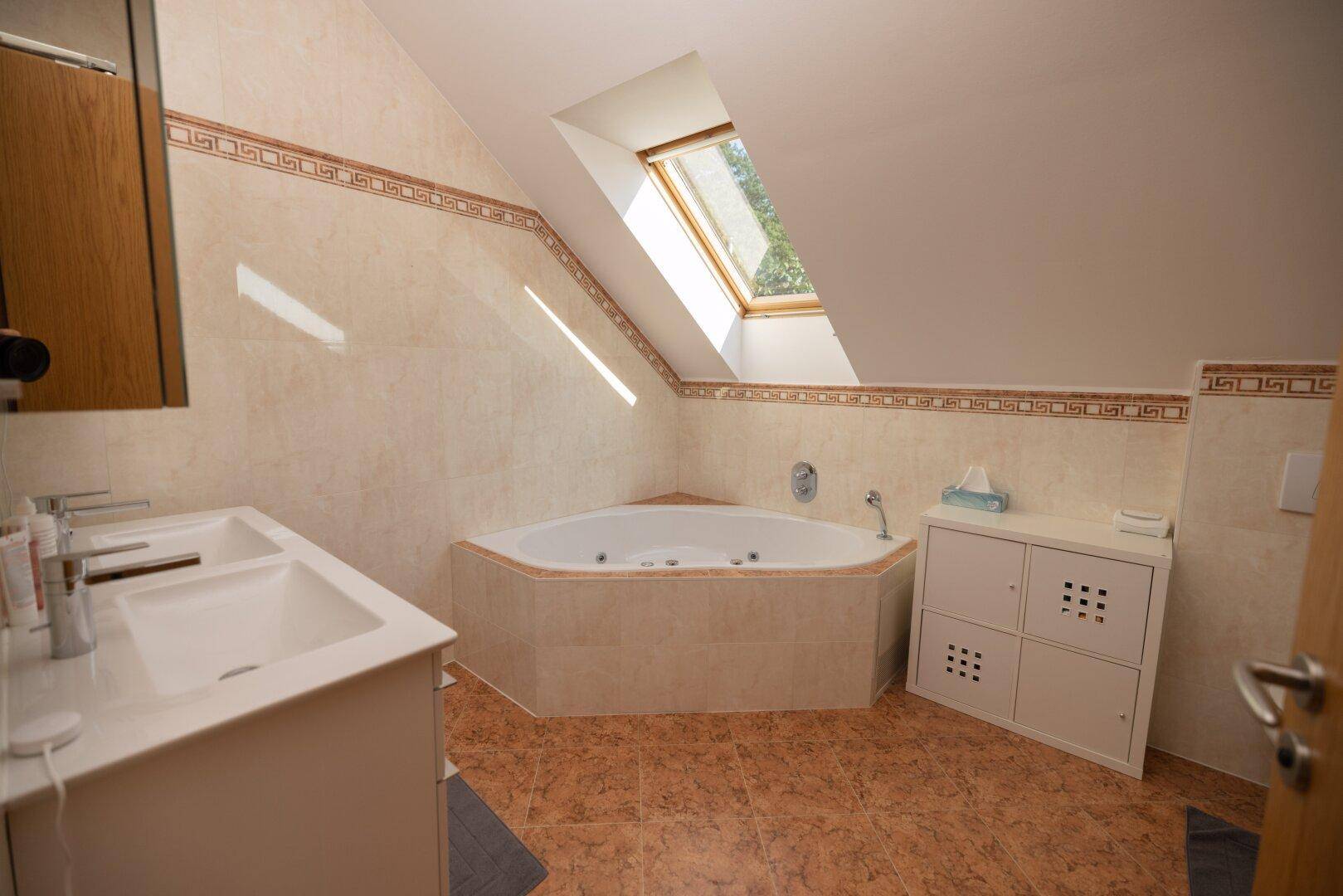 Badezimmer mit Eckbadewanne, Doppelwaschbecken und Dachfenster für natürliches Licht.