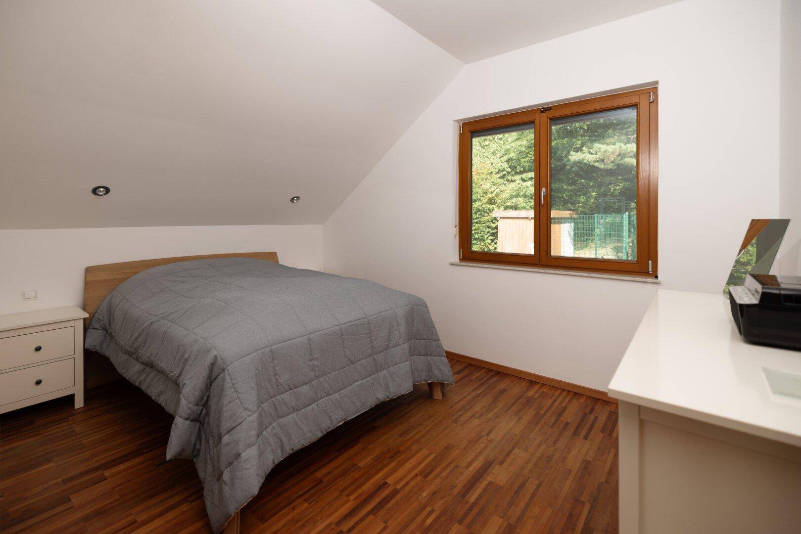 Schlafzimmer mit Holzboden, Doppelbett und Fenster mit Blick ins Grüne.