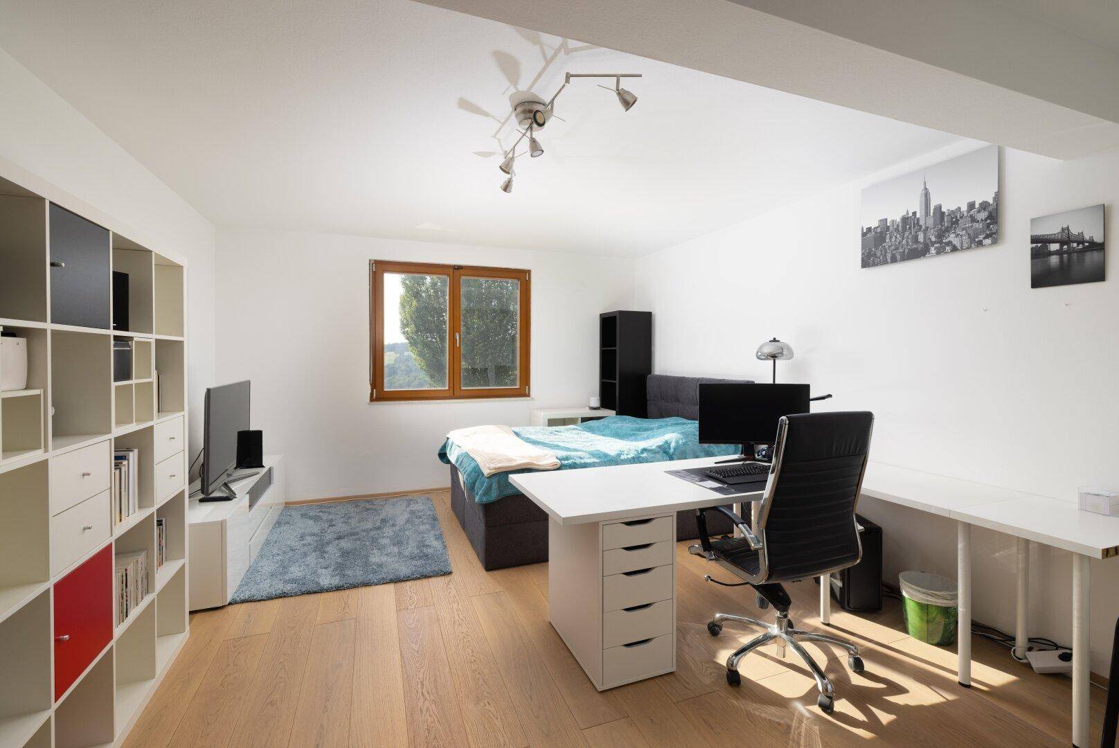 Geräumiges Schlafzimmer mit Arbeitsbereich, hellem Boden und Blick ins Grüne.