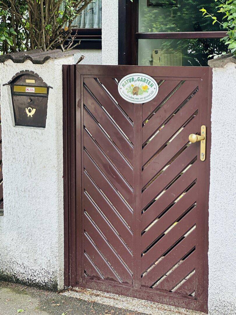 Nahaufnahme des Gartentors mit einem "Natur Garten" Schild und einem Briefkasten.