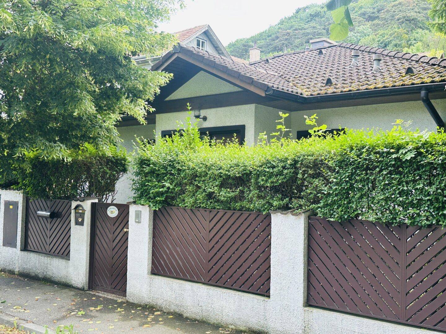 Fassade des Hauses von der Straße aus gesehen, umgeben von einer Hecke und einem Holzzaun.