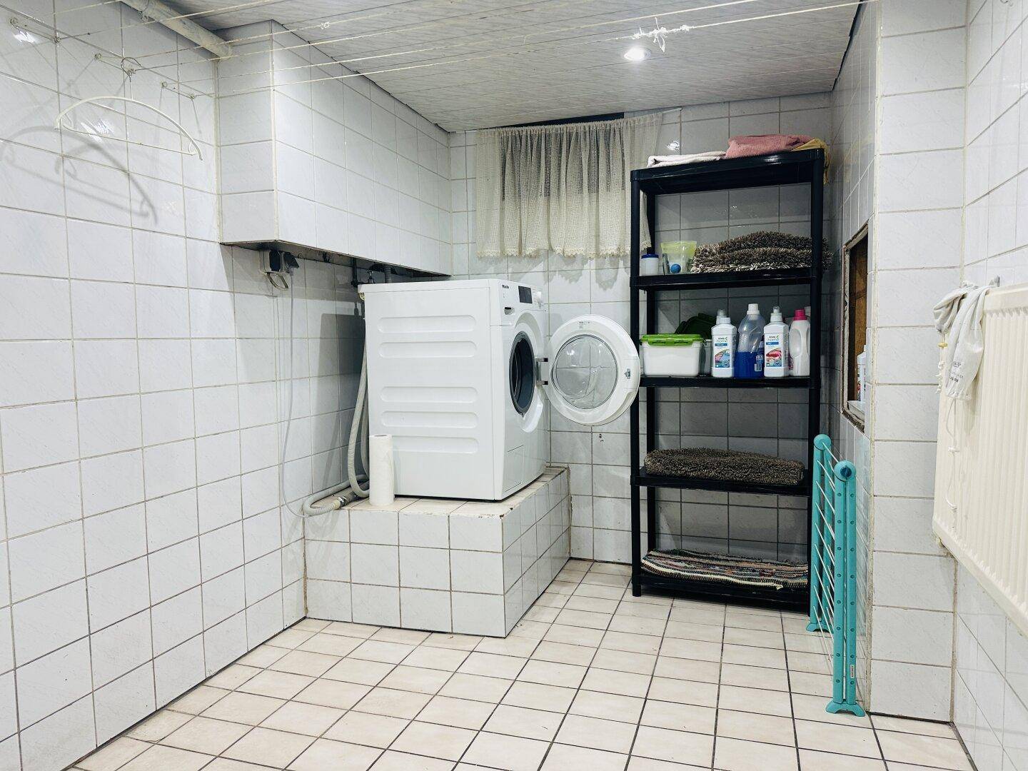 Praktischer Hauswirtschaftsraum im Keller mit Waschmaschine und Fliesen an Wänden und Boden.
