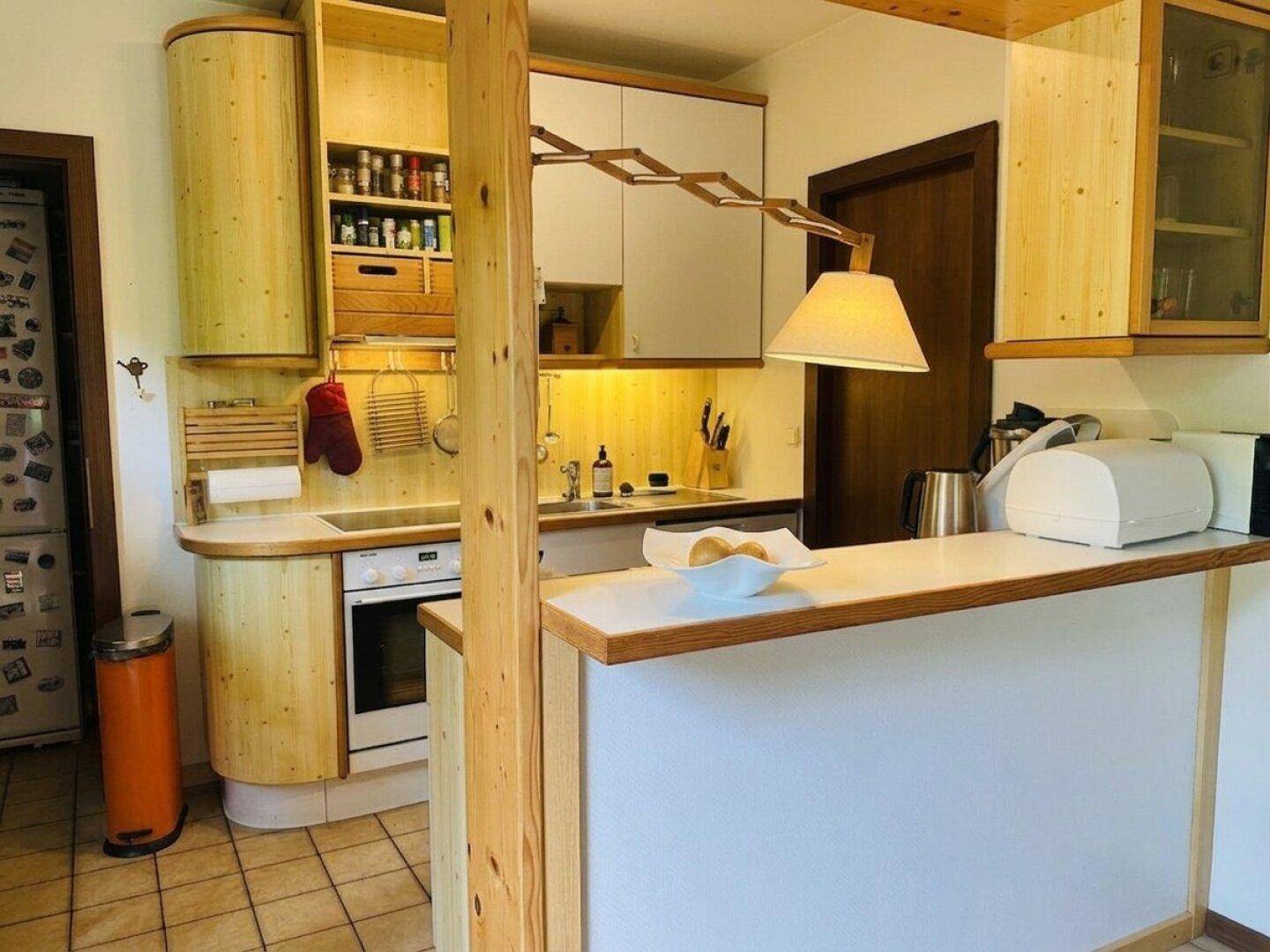 Helle Küche mit Holzschränken, weißer Arbeitsplatte und kleiner Frühstücksbar, offen gestaltet.