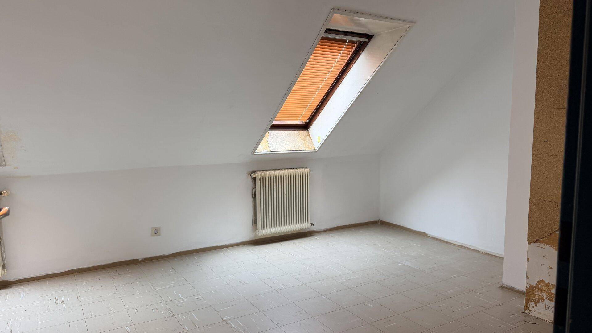 Dachgeschossraum mit schrägen Wänden und Dachfenster, bietet viel natürliches Licht.