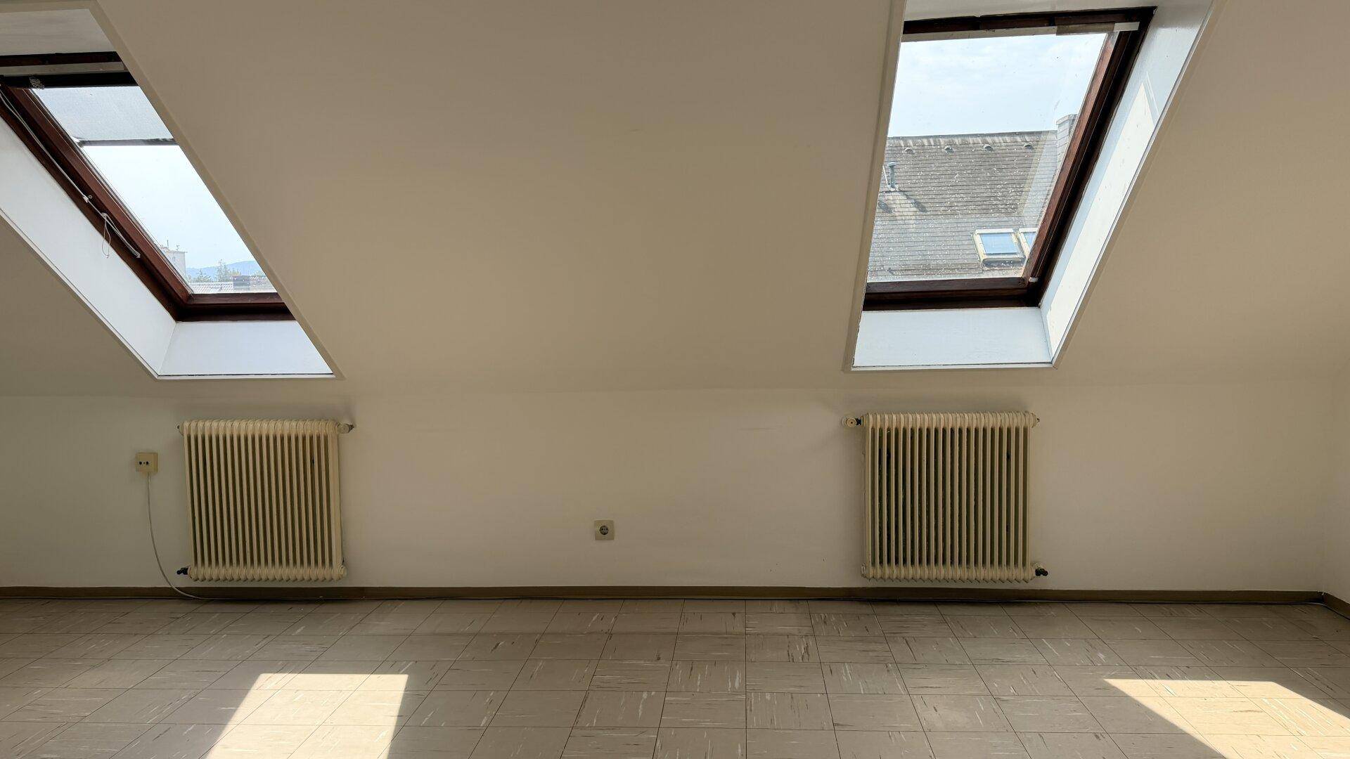 Heller Dachgeschossraum mit zwei großen Dachfenstern, die den Raum mit Licht durchfluten.