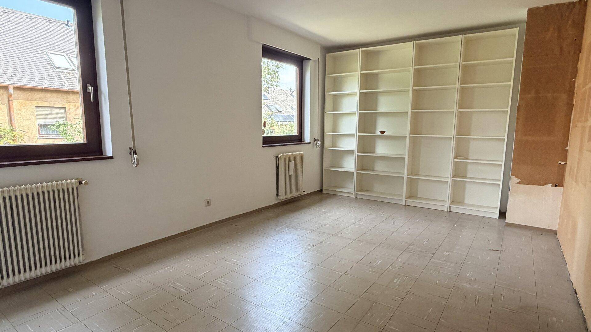 Geräumiger Raum mit großen Fenstern und integrierten Bücherregalen, ideal als Wohn- oder Arbeitsbereich.