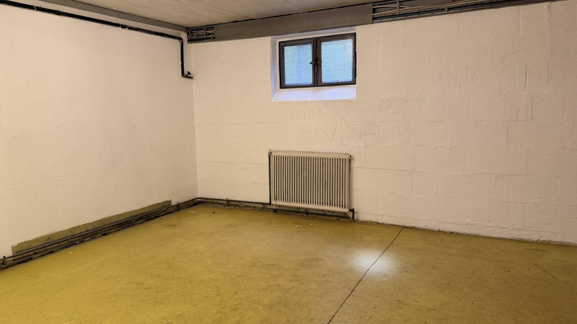 Geräumiger Kellerraum mit kleinem Fenster und gelbem Boden, ideal als Abstellfläche.