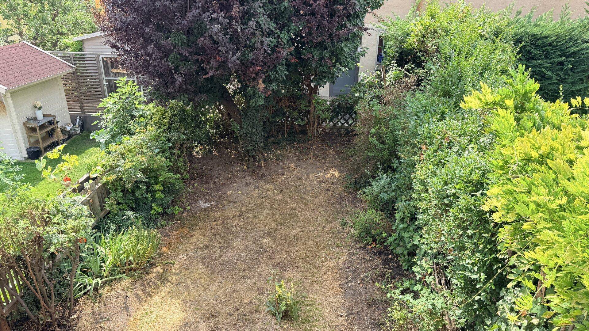Gepflegter Gartenbereich mit üppiger Bepflanzung und einem kleinen Gartenhaus im Hintergrund.