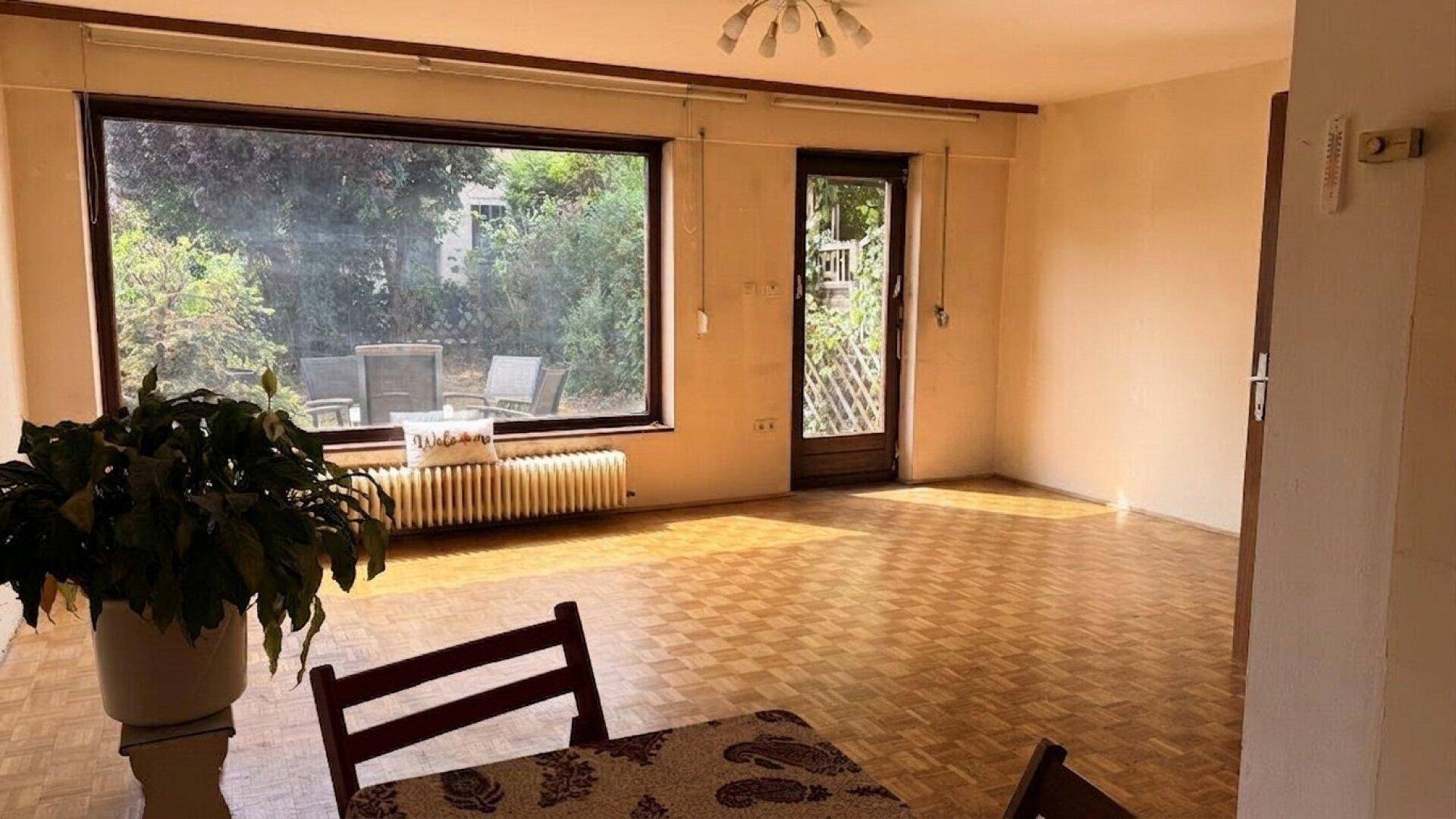 Helles Wohnzimmer mit Parkettboden und großem Fenster mit Blick in den Garten.