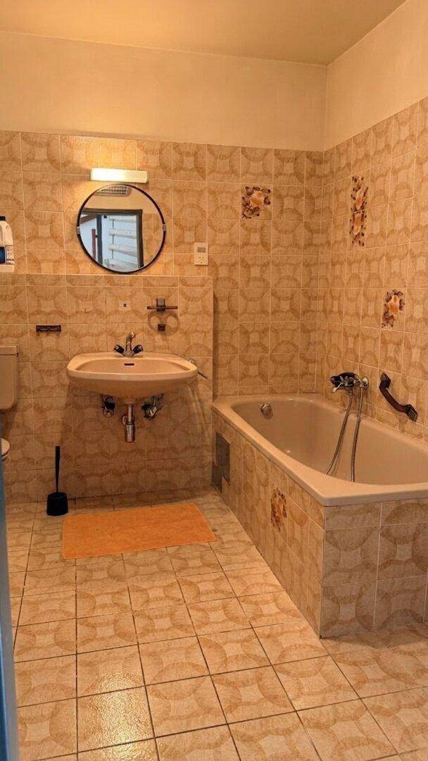 Badezimmer mit beigefarbenen Fliesen, Badewanne und Waschbecken, in gutem, aber älterem Zustand.