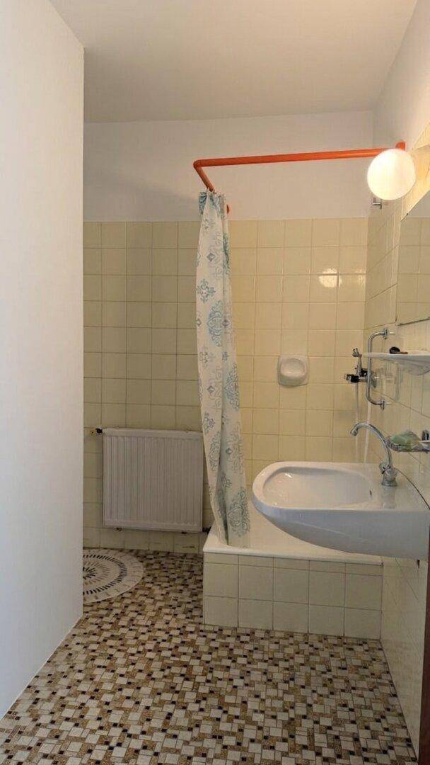 Badezimmer mit Duschbereich und Mosaikfliesen, in einem funktionalen, aber älteren Zustand.