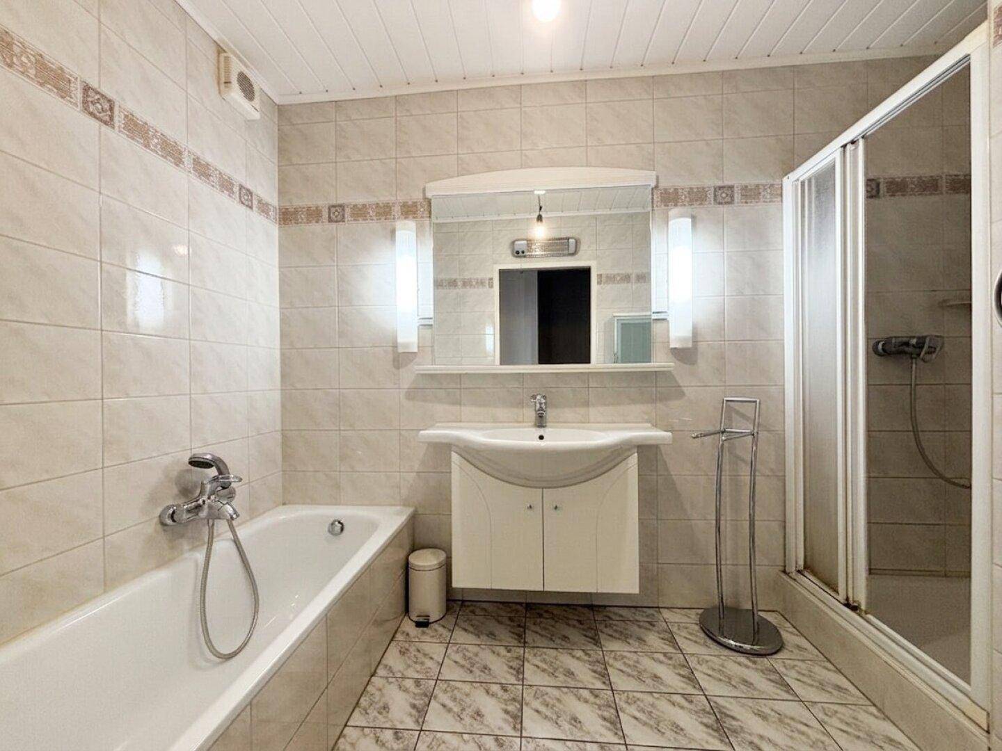 Gefliestes Badezimmer mit Badewanne, Duschkabine und modernem Waschtisch.