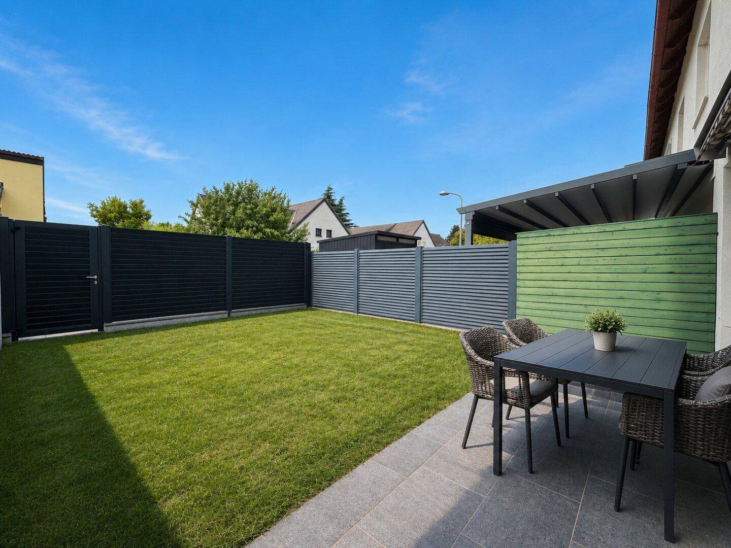 Gepflegter Garten mit Rasenfläche, moderner Terrasse und Essbereich im Freien.