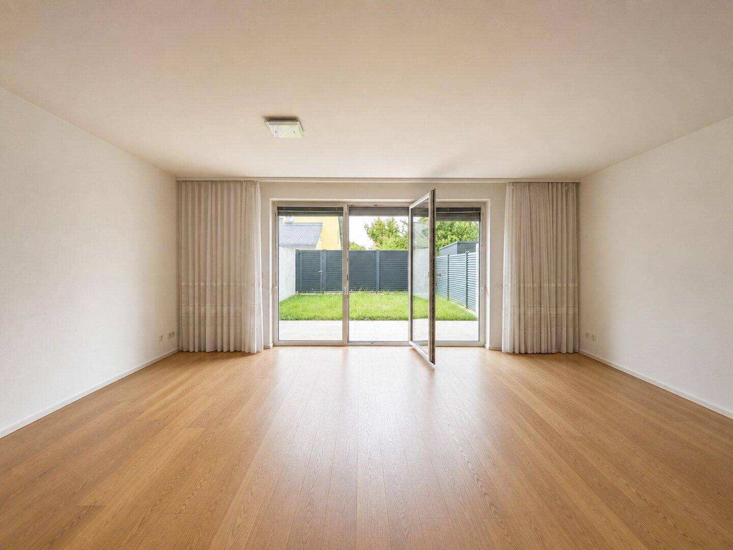 Heller Raum mit Holzboden und großen Glastüren, die zum Garten führen.