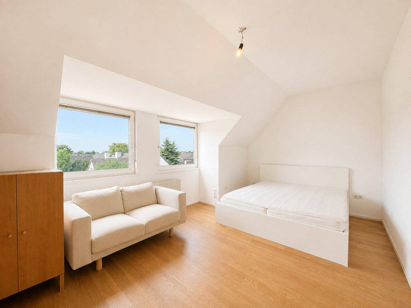 Helles Schlafzimmer im Dachgeschoss mit Schrägen, Holzboden und Blick ins Grüne.