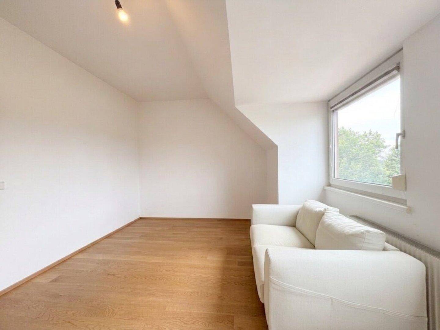 Gemütlicher Raum im Dachgeschoss mit Sofa, Holzboden und Fenster für natürliches Licht.