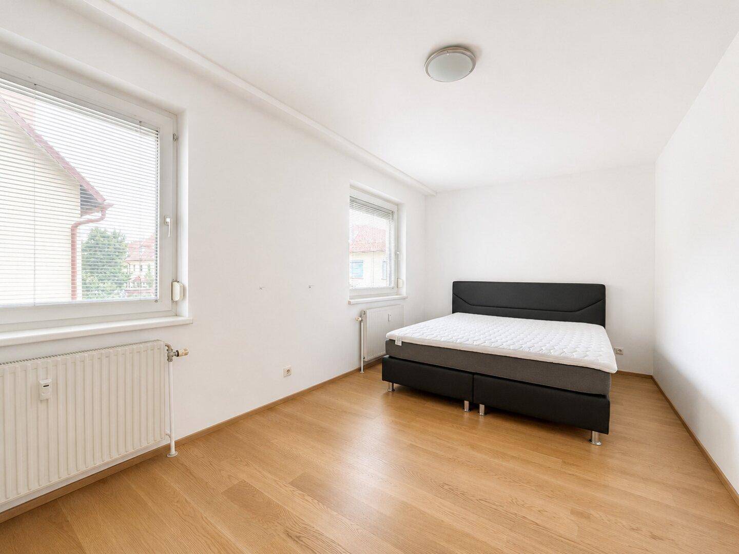 Komfortables Schlafzimmer mit Doppelbett, Holzboden und zwei Fenstern für viel Licht.