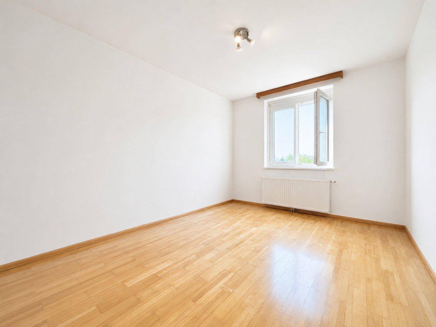 Freundliches Schlafzimmer mit Holzparkettboden und großem Fenster für viel Tageslicht.