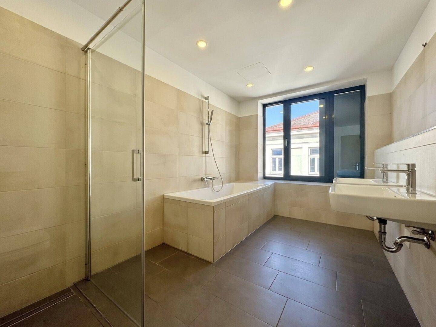 Modernes Badezimmer mit Badewanne, Dusche, Doppelwaschbecken und Fenster.