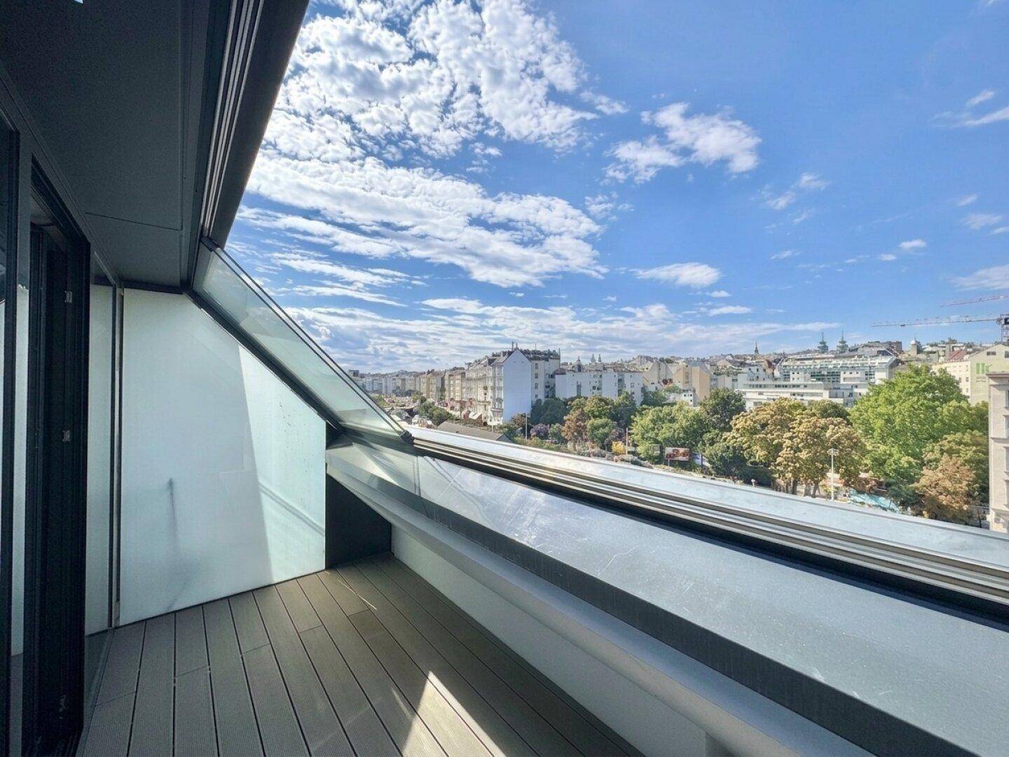 Sonniger Dachschrägenbalkon mit Holzdielen und weitem Blick über die Stadt.