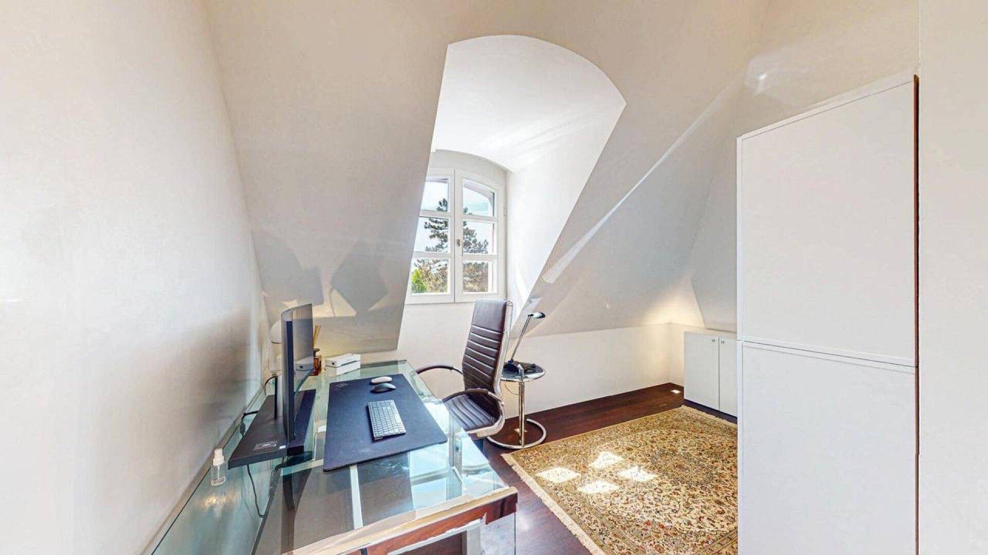 Arbeitszimmer im Dachgeschoss mit Schreibtisch, Teppich und charakteristischer Dachschräge.