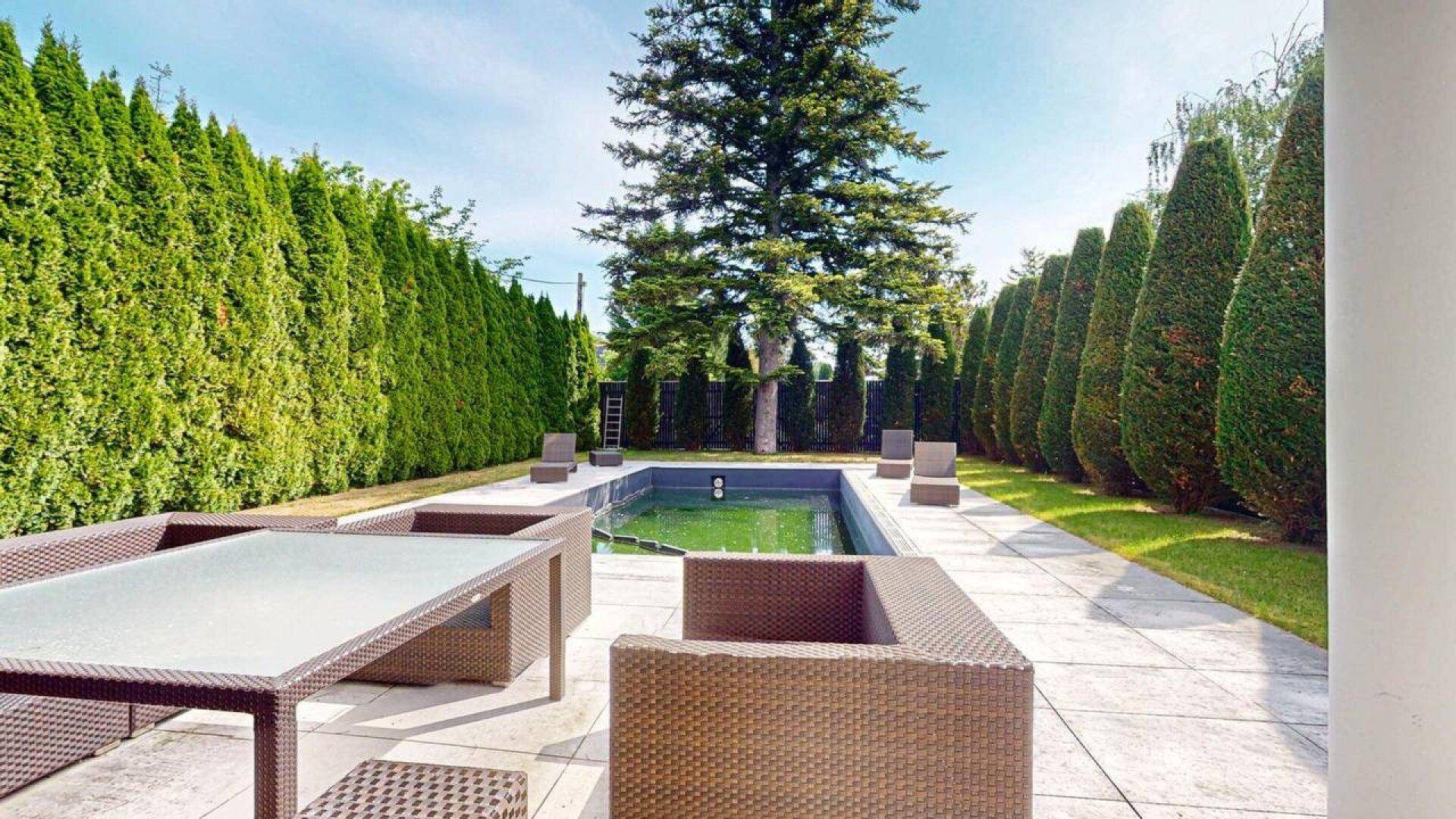 Großer Poolbereich mit gepflasterter Terrasse, Outdoor-Möbeln und hohen Hecken.