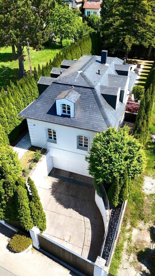 Luftaufnahme der Villa mit Einfahrt, Garage und Mansarddach in grüner Umgebung.