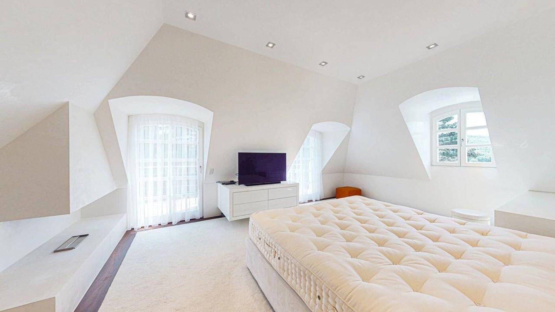 Helles Schlafzimmer im Dachgeschoss mit Teppichboden, Dachschrägen und Fenster.