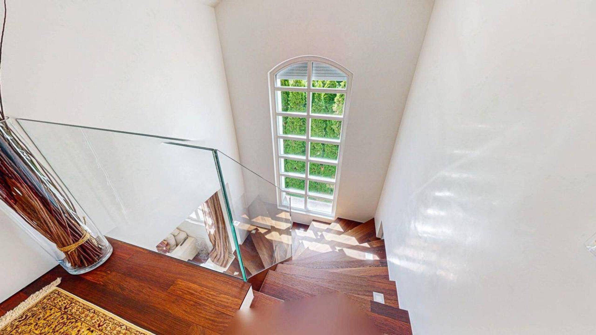 Elegante Holztreppe mit Glasgeländer und großem Fenster für viel Tageslicht.
