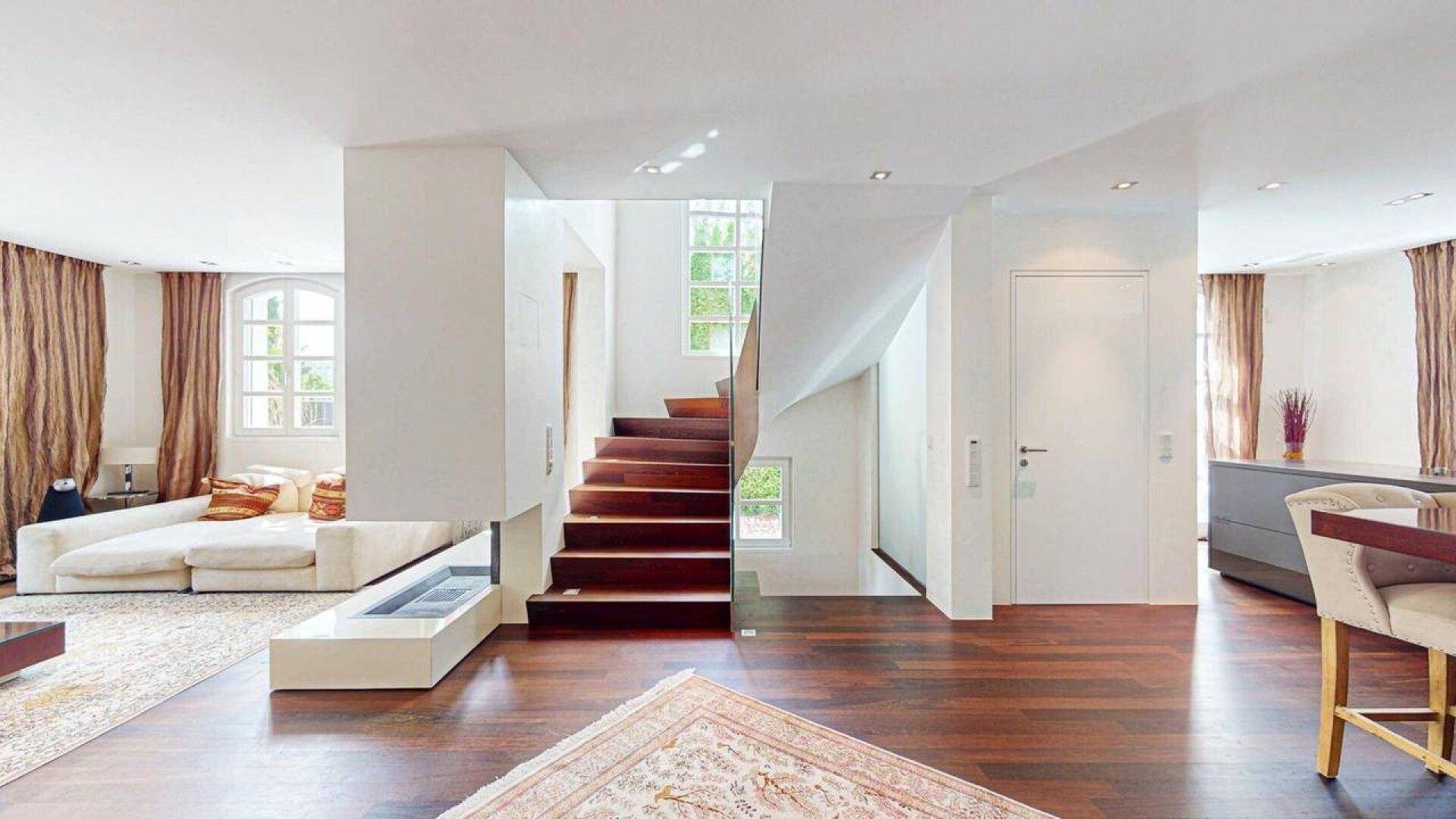 Heller, offener Wohnbereich mit eleganter Holztreppe, modernem Kamin und hochwertigem Parkettboden.