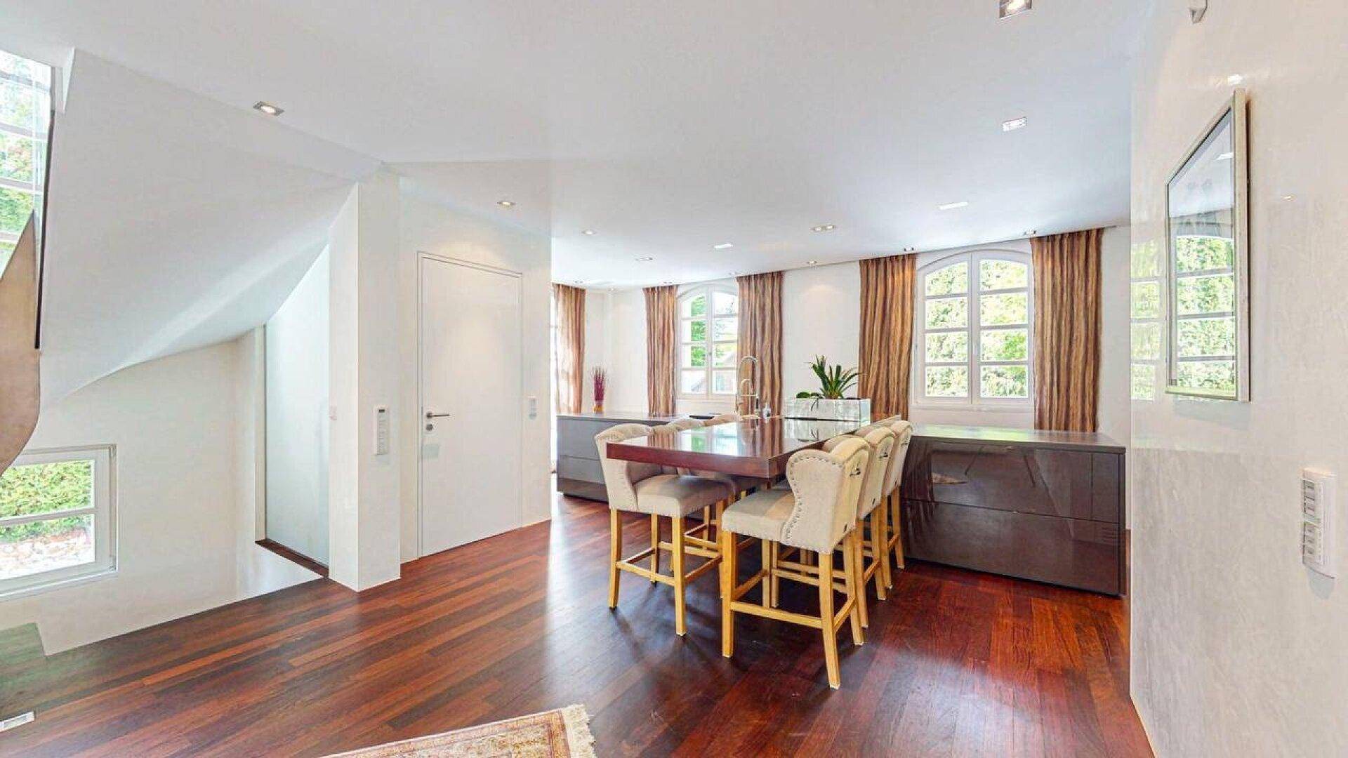 Eleganter Essbereich mit großem Holztisch, bequemen Stühlen und Blick auf die Treppe und Fenster.