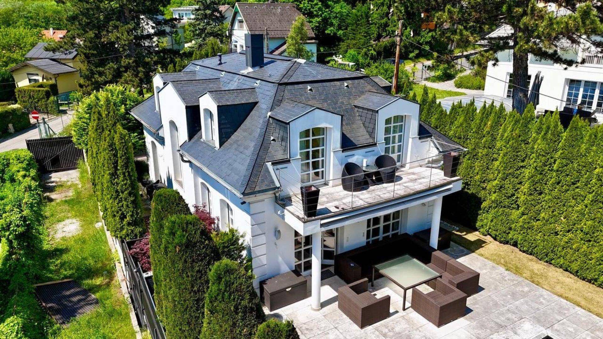 Luftaufnahme des eleganten Hauses mit Mansarddach, großem Balkon und gepflegtem Gartenbereich.