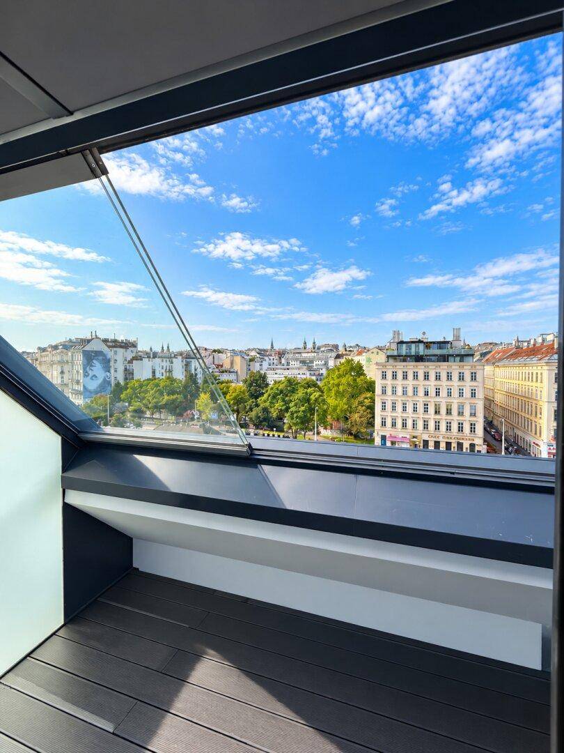 Panoramablick über die Stadt durch ein großes Schrägfenster mit blauem Himmel.