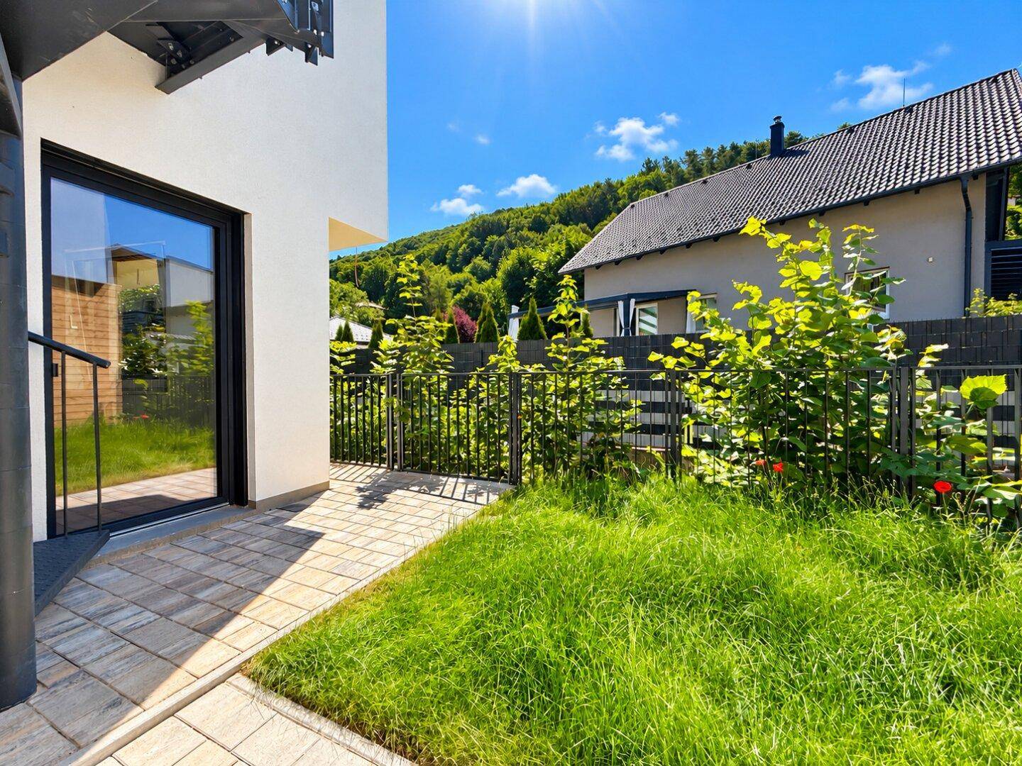 Kleiner Gartenbereich mit Rasen und gepflastertem Zugang zu einer modernen Glastür des Hauses.