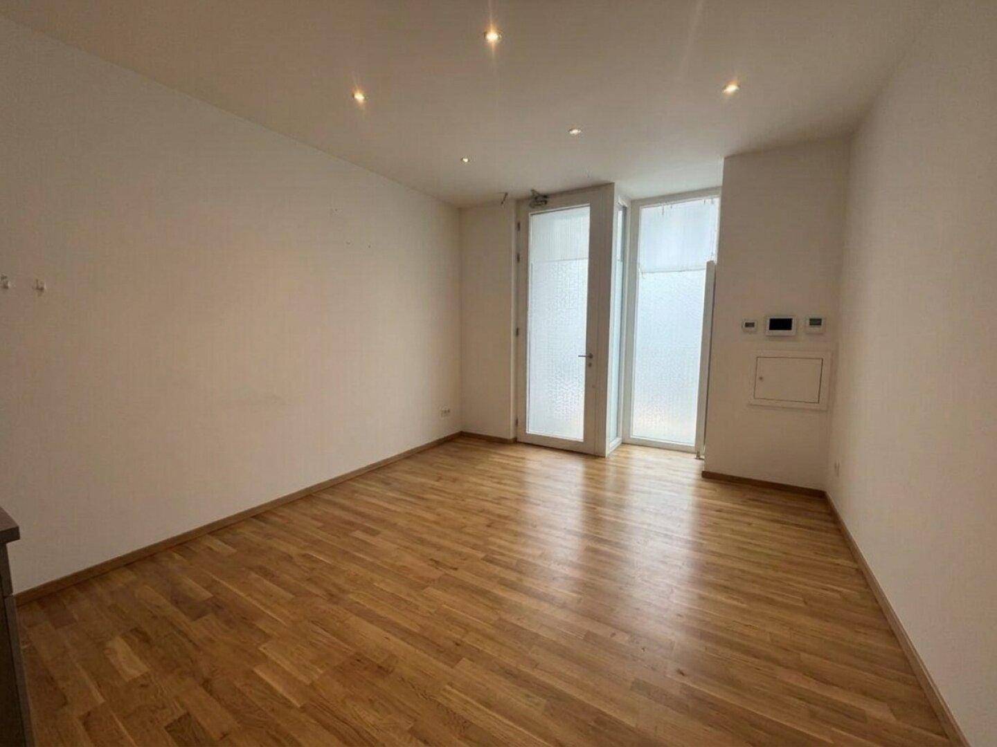 Geräumiger, unmöblierter Raum mit Holzboden und weißen Wänden, ausgestattet mit modernen Deckenspots.